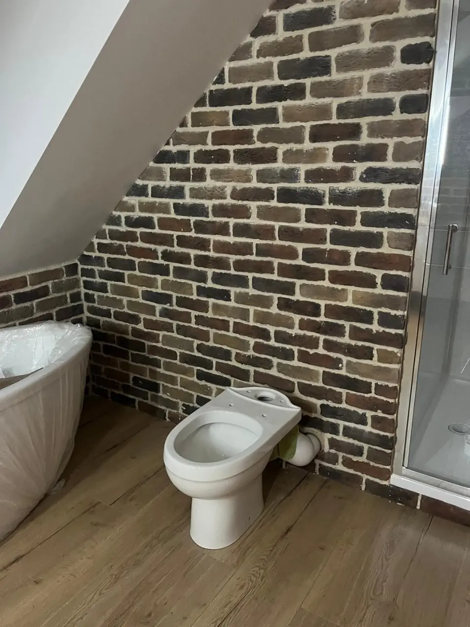 Toilet fitted beneath the sloping ceiling beside the brick feature wall