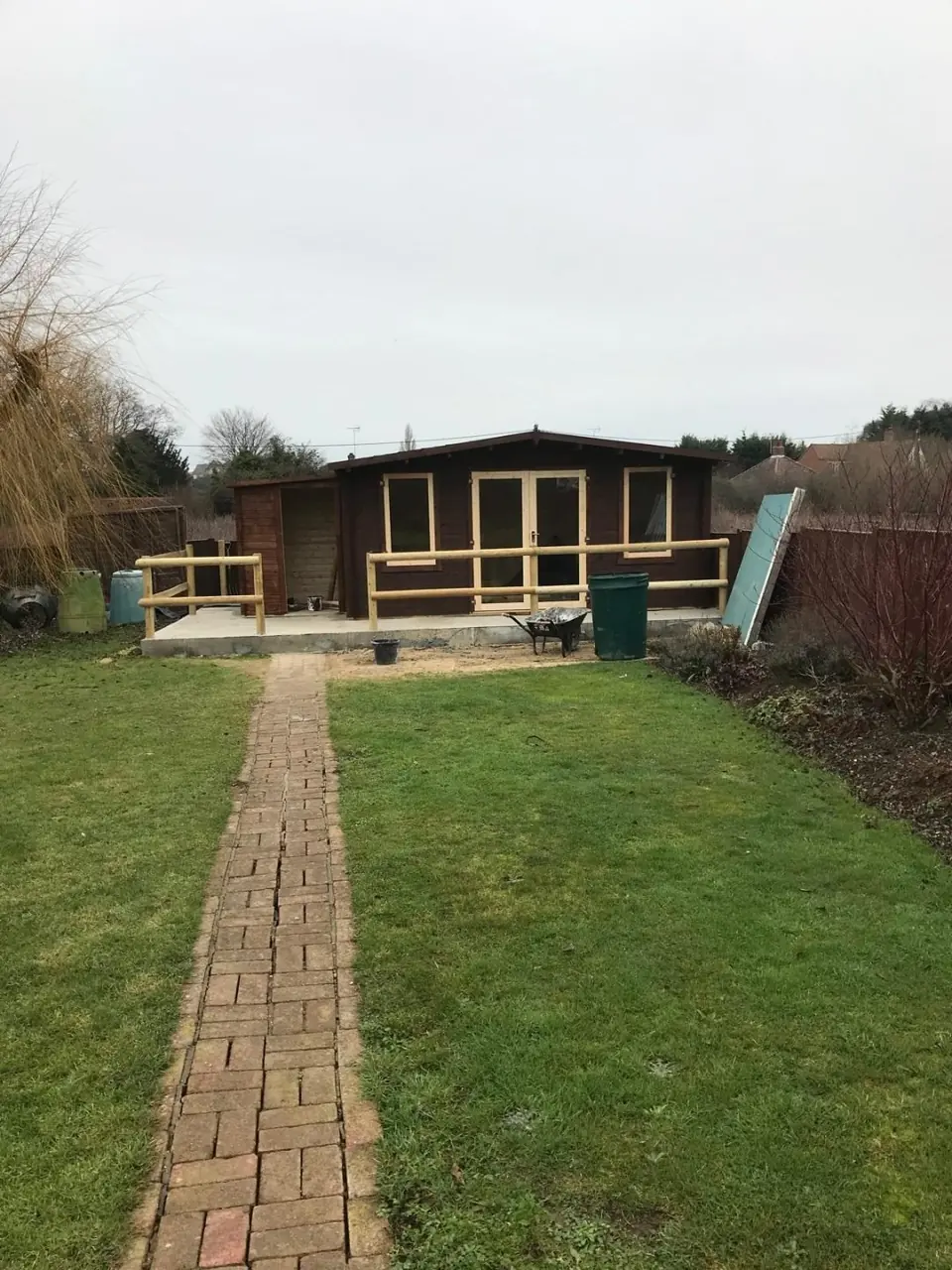 Completed log cabin office at the end of the garden, with a brick path across the lawn