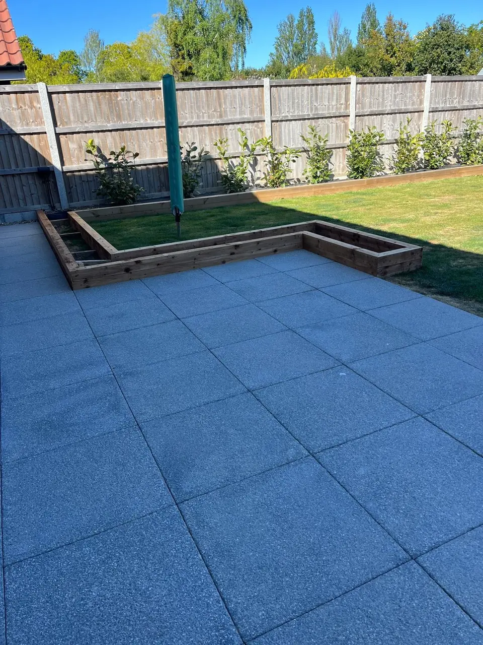 Finished grey paved patio with timber-edged borders and evergreen planting beside the lawn