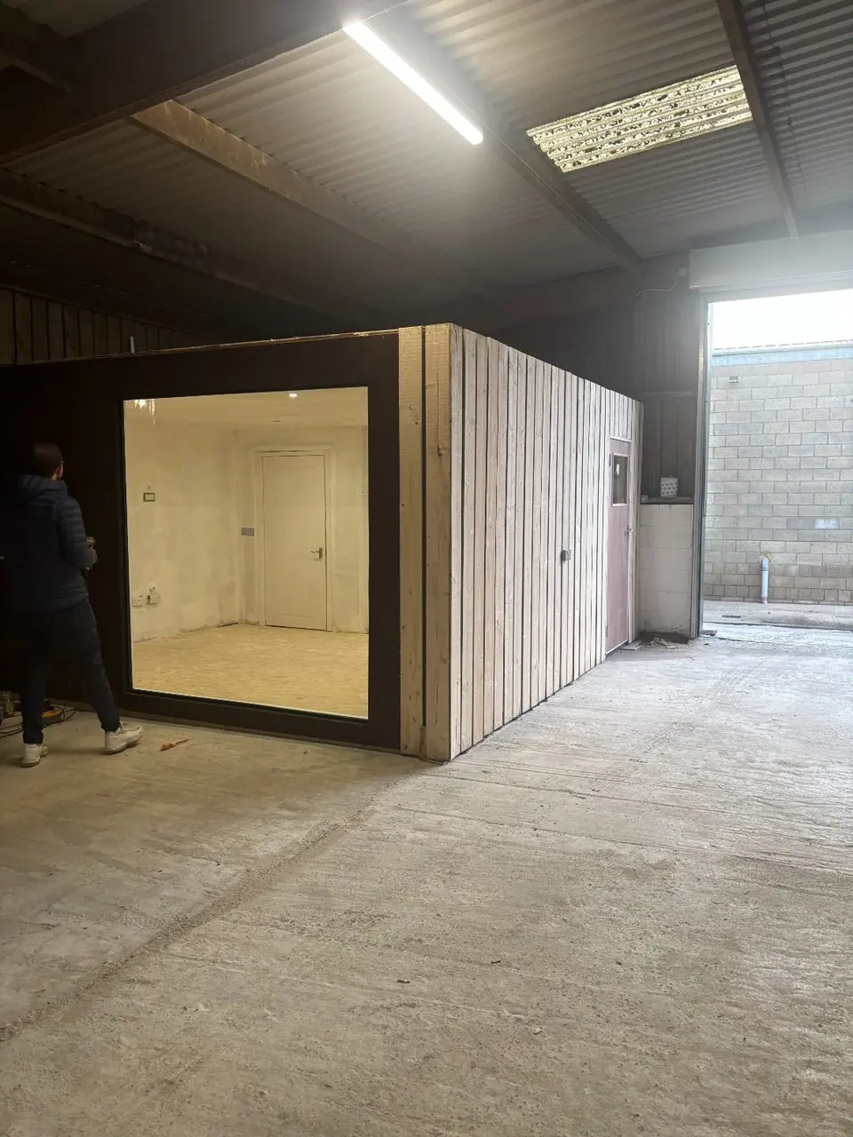 Timber-clad office pod with its glazed front installed inside the workshop
