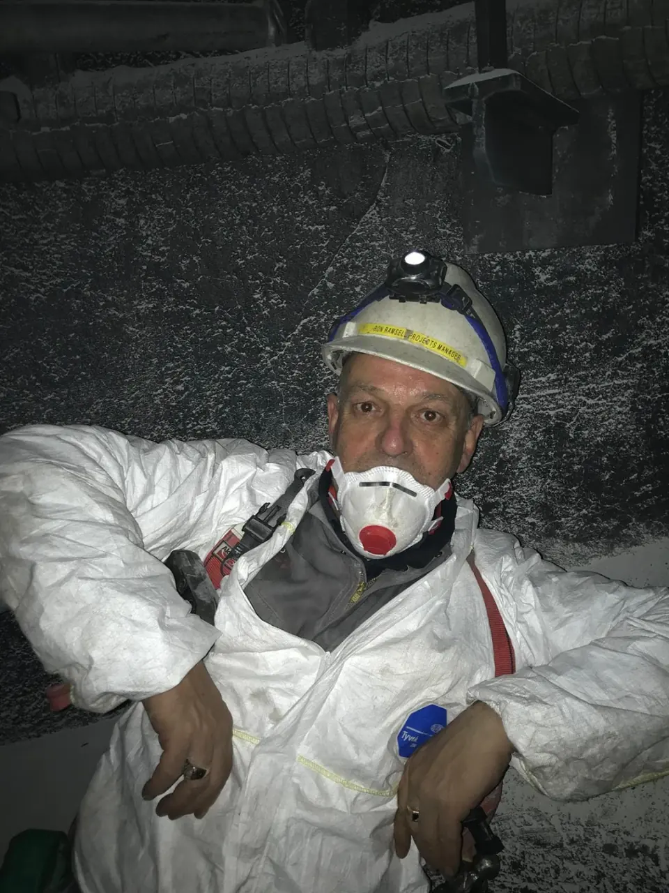 Ron Ramsell in a hard hat, mask and protective suit inside an industrial vessel
