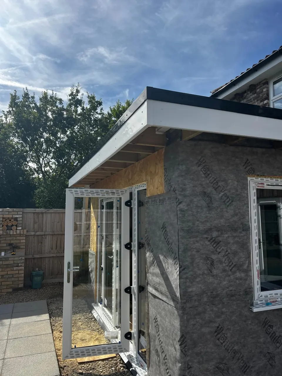 Corner of the extension with fitted glazing, white fascia and exposed wall membrane