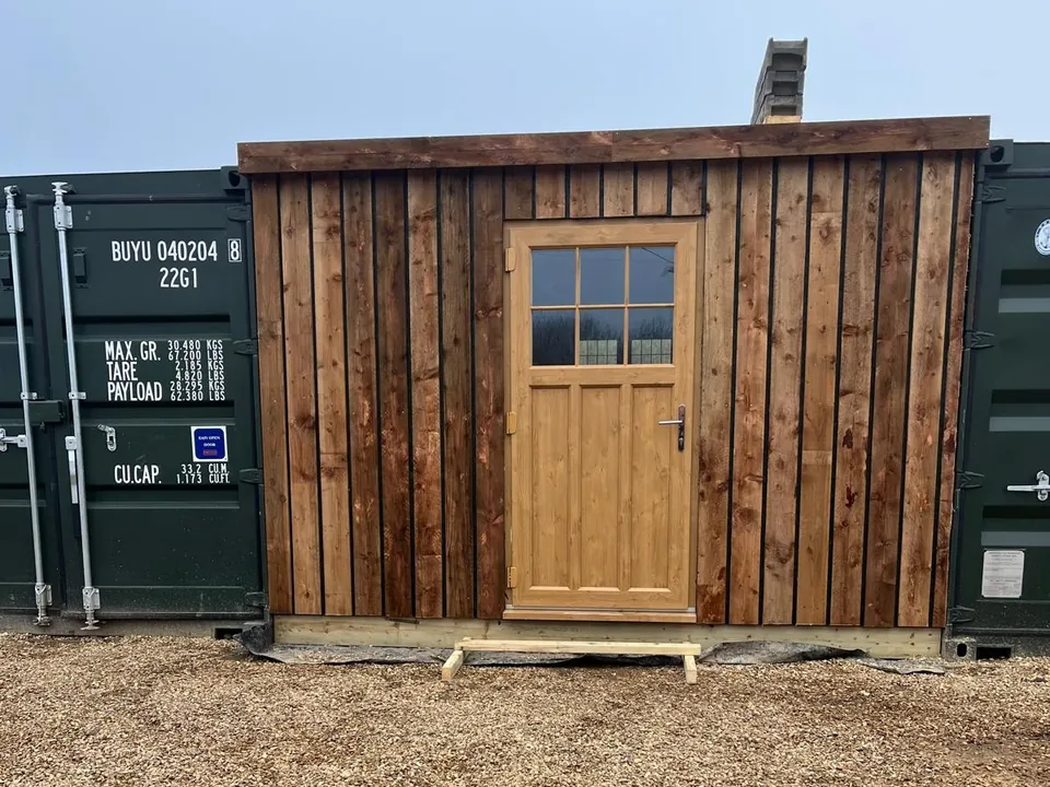 Completed timber-clad frontage and glazed door fitted between two shipping containers