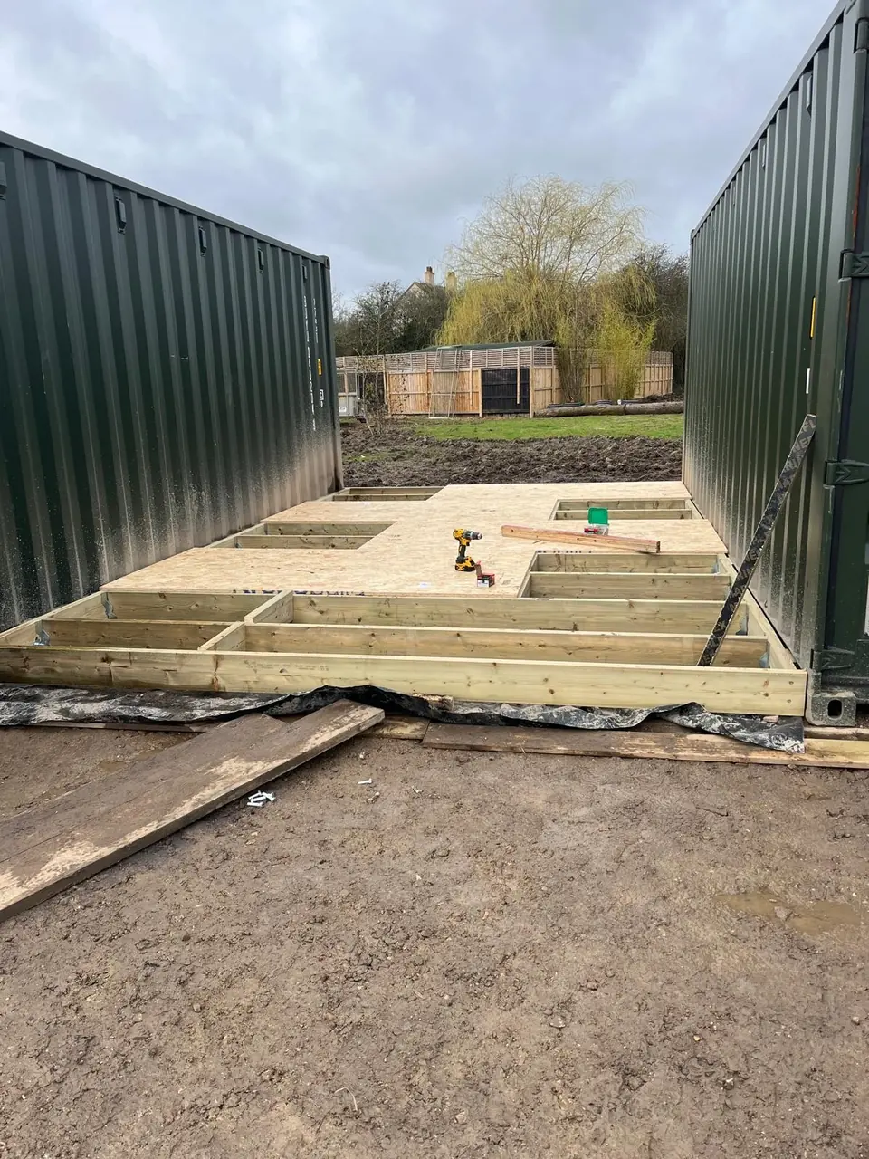 Timber floor frame and OSB decking under construction between two shipping containers